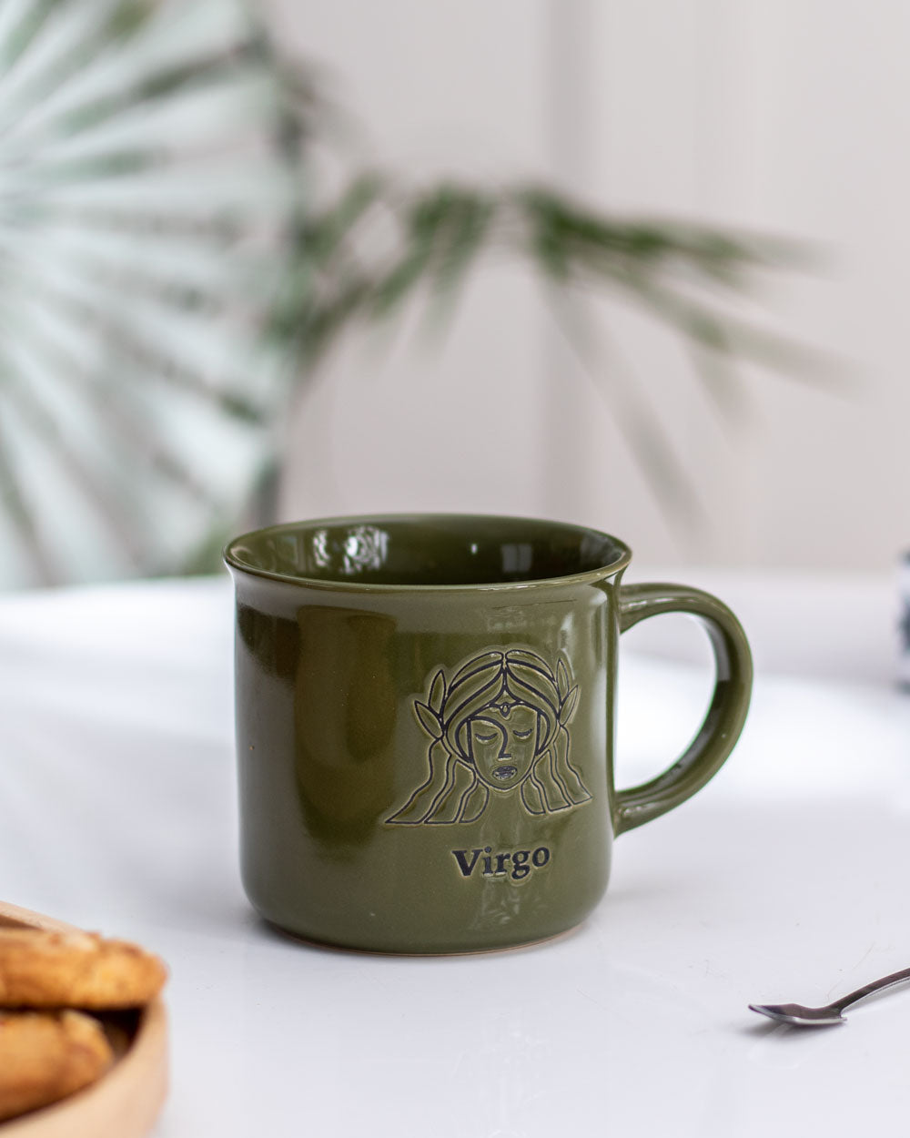 Virgo astrological sign mug in a soothing green hue with a golden design, creating a serene coffee experience, against a blurred plant backdrop.