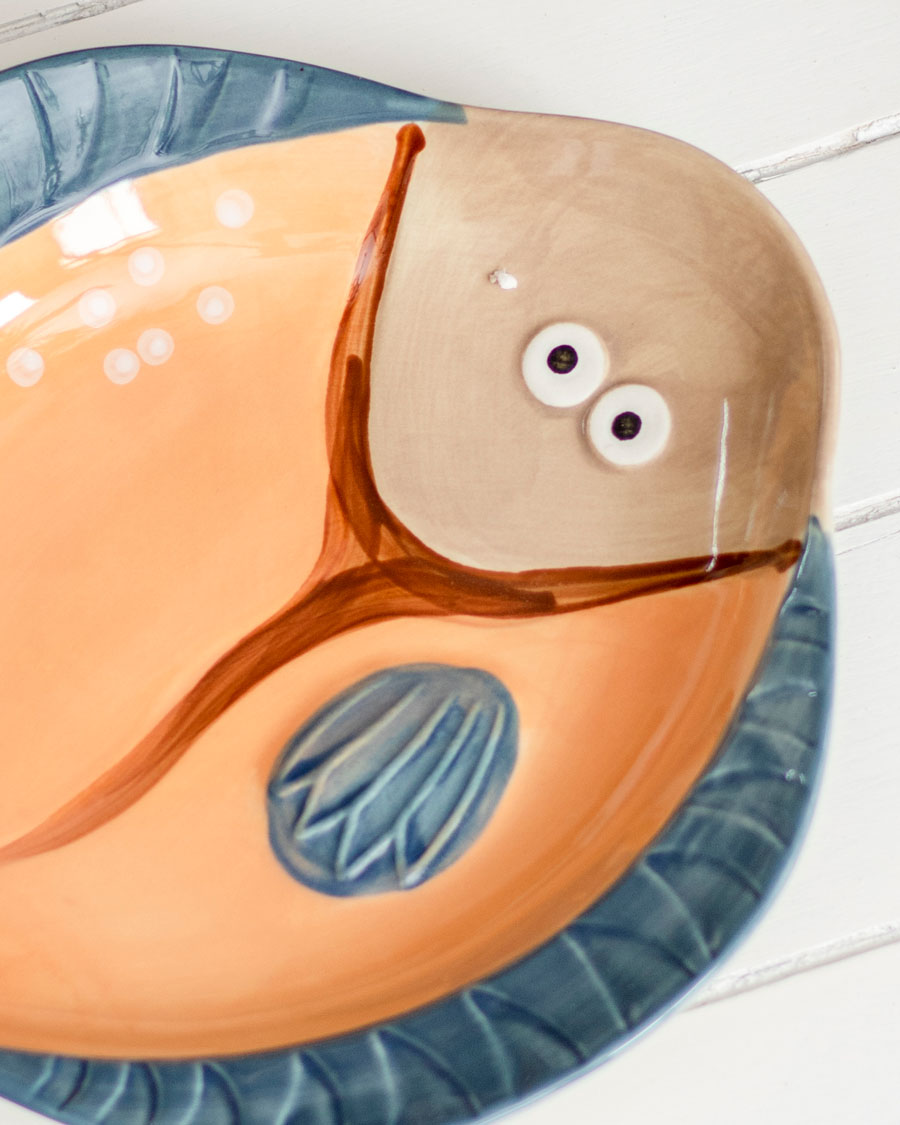 Close-up of orange and blue Gilligan fish-shaped ceramic platter with decorative eye detail.
