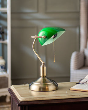 Electric table lamp that has a brass stand, a green glass lamp shade and a pull-chain switch.