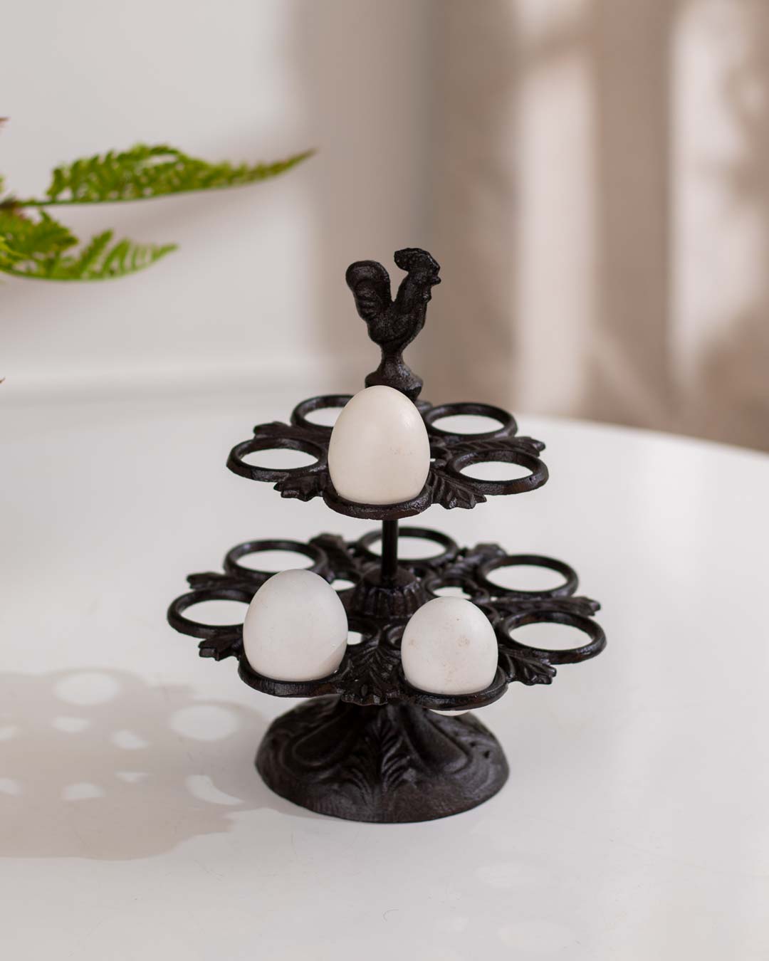 Ornate cast iron bird feeder with multiple rings and bird figurines, mounted on a wooden post in a lush garden.