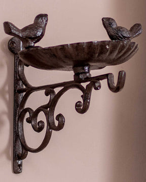 Decorative bird feeder crafted from cast iron with a classic patina finish, mounted on a beige wall.