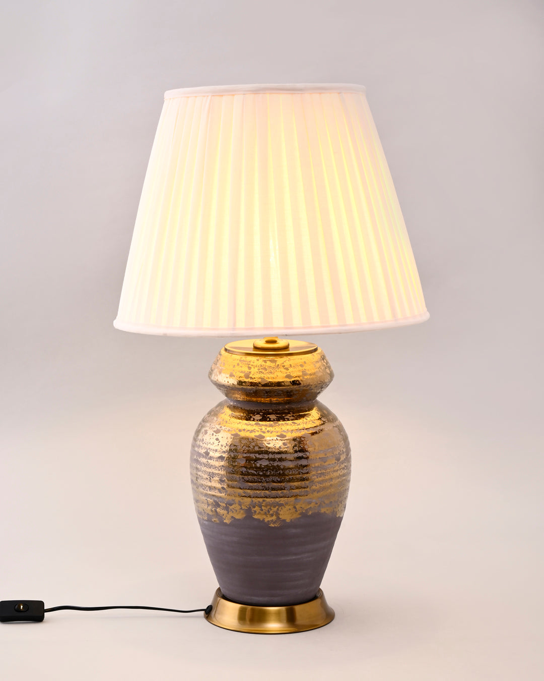 Table lamp with a textured ceramic base and pleated white shade on a light gray background