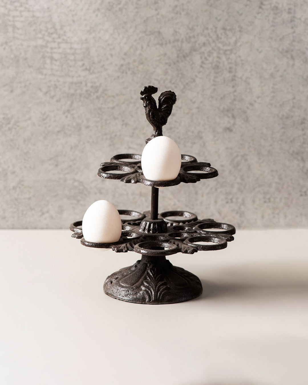 Rooster-topped cast iron egg holder with intricate base design holding a single egg.