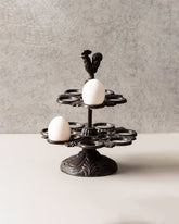 Rooster-topped cast iron egg holder with intricate base design holding a single egg.