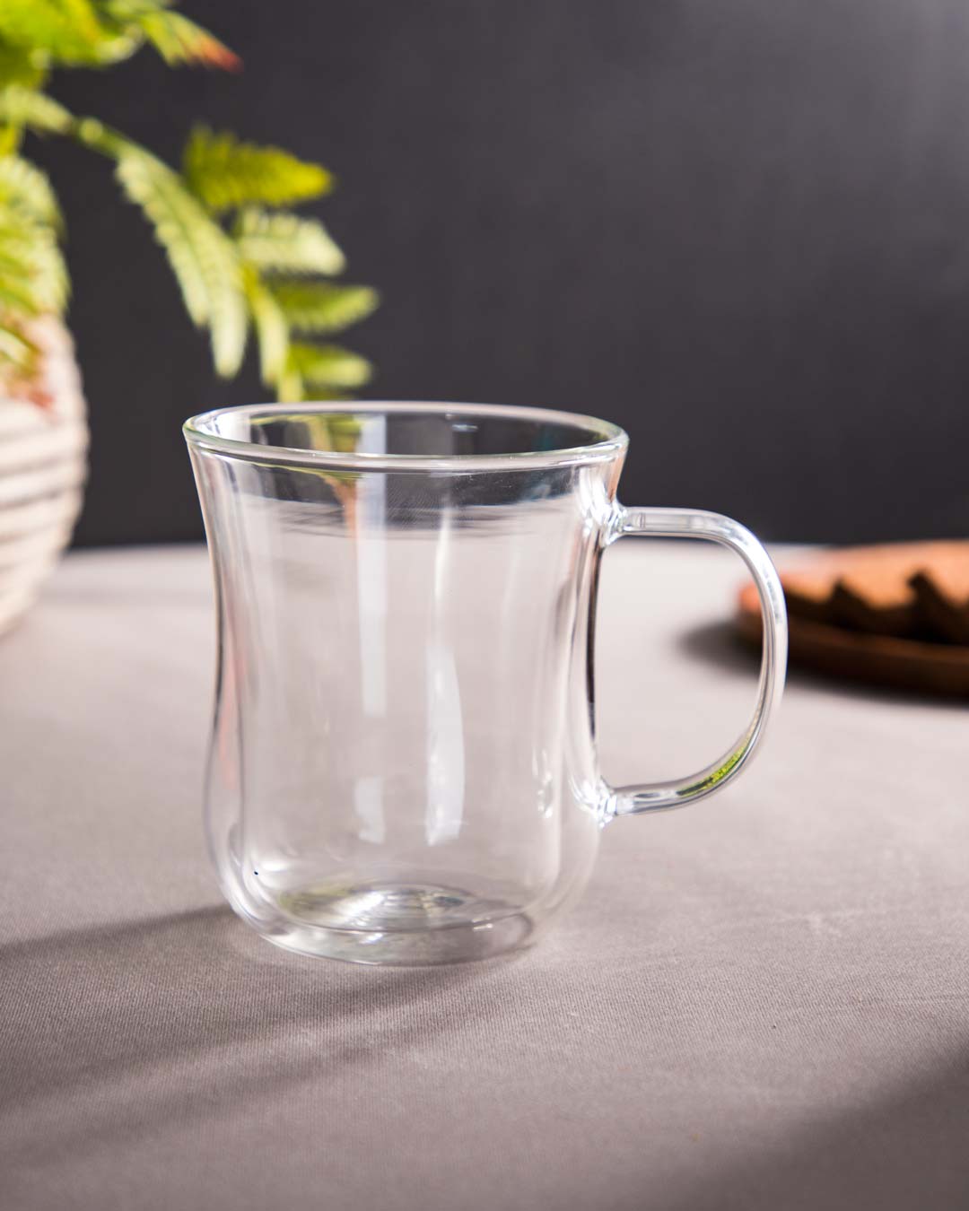 Clear thermal double-walled glass tea cup on a table with a fern in the background.