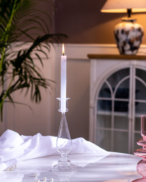 Elegant table centerpiece with a transparent glass candlestick holder and a lit candle providing a warm ambiance in a dimly lit room.