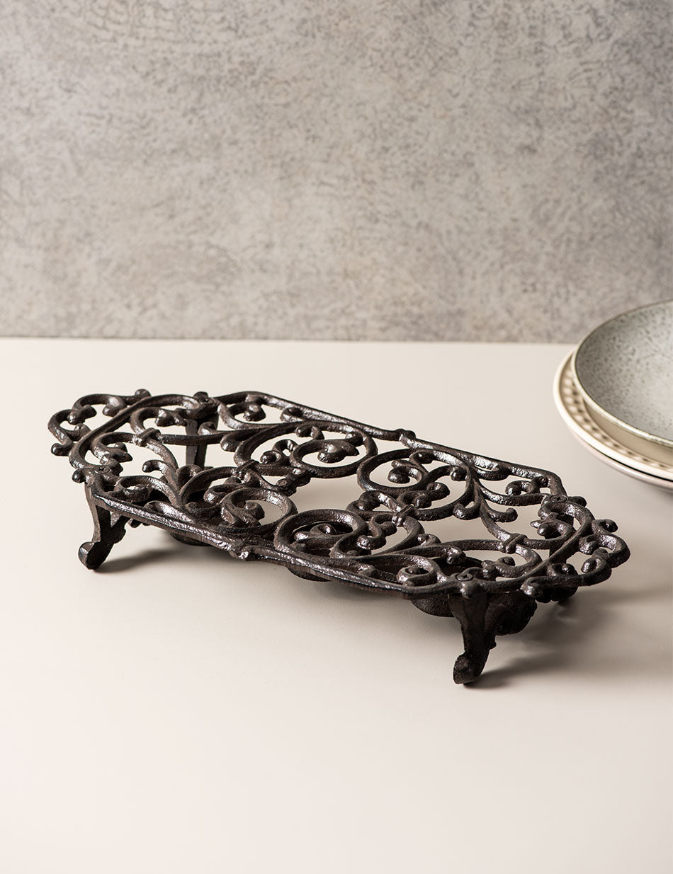 Antique black cast iron trivet for dish warming, with an elegant ornamental design. 