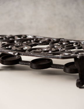 Close-up of a vintage-style cast iron trivet, featuring ornate craftsmanship. 
